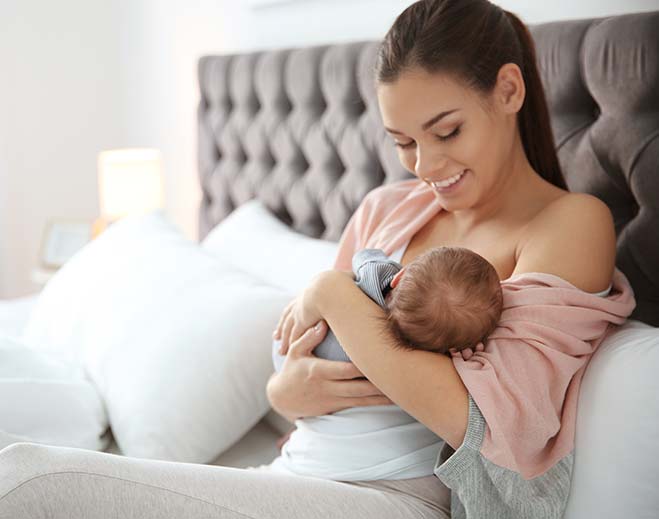 mother breastfeeding baby on bed